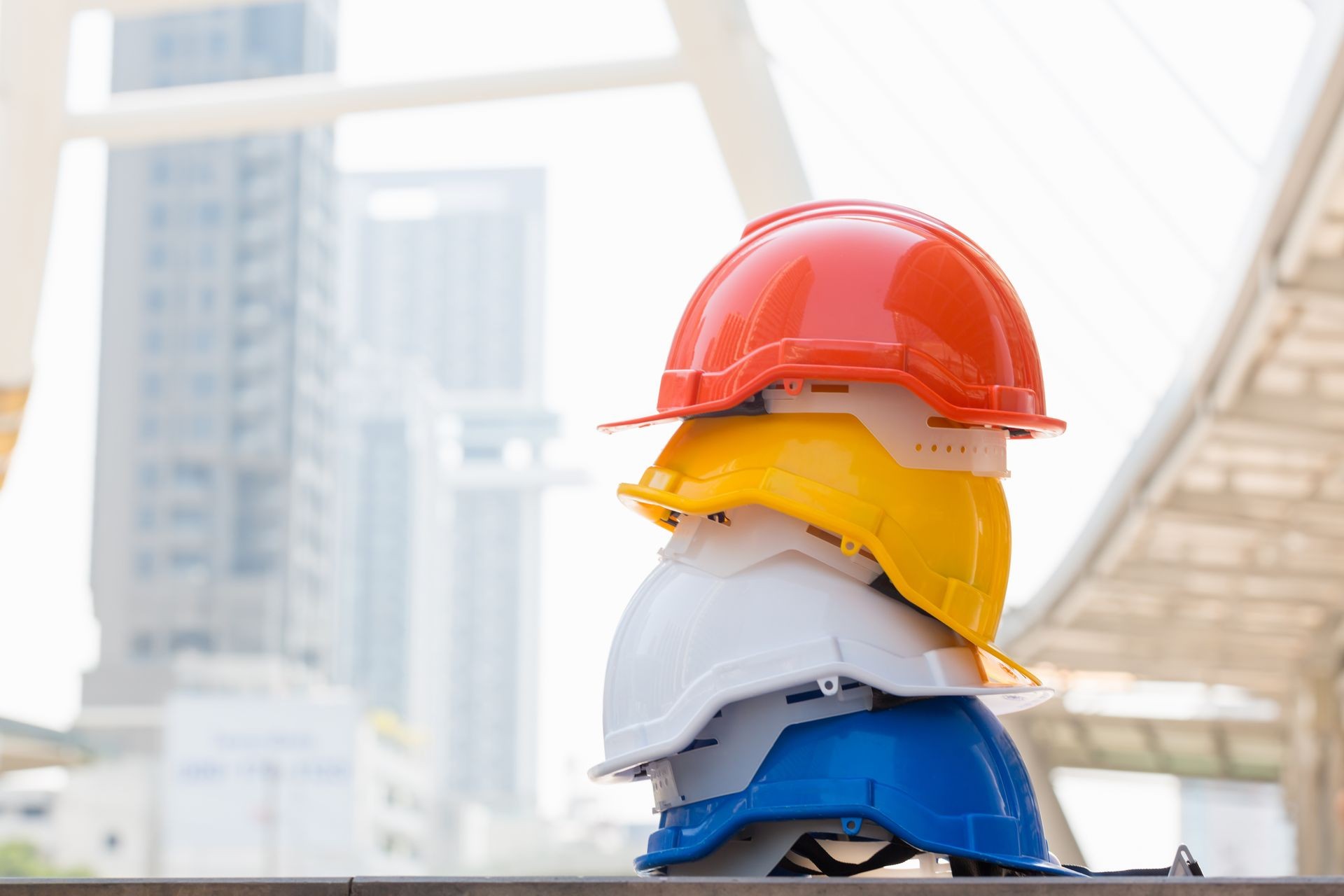 Orange, blue, white, and yellow hard safety helmet hat for safety project on the big building in city / Safety first concept. Orange, blue, white, and yellow hard safety helmet hat for safety project on the big building in city / Safety first concept.